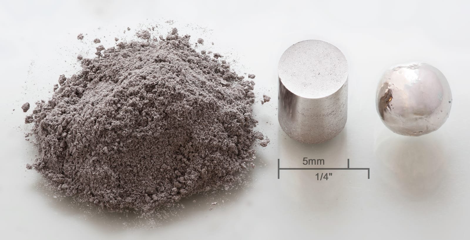 Illustrative image: three small samples of rhodium metal, as powder, a pressed cylinder and a melted pellet.
